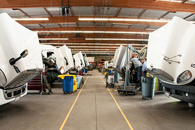 Semi trucks sit parked with their hoods open and ready to be worked on in the service shop at …